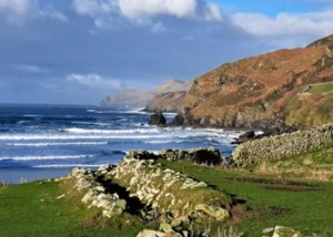 Green fields along coastline with stone wall in the foreground and sea with cliffs in the background