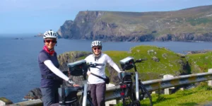 Two cyclists standing with bicycles at coastline with cliffs in the background.