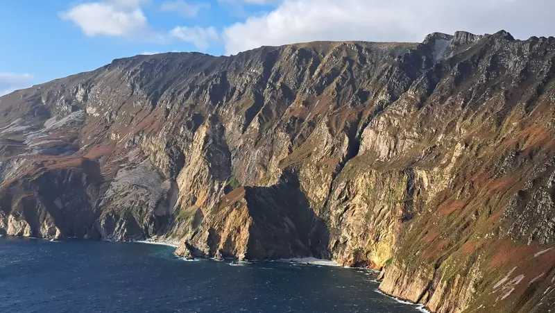 Cliffs dropping into the sea with partly cloudy sky.