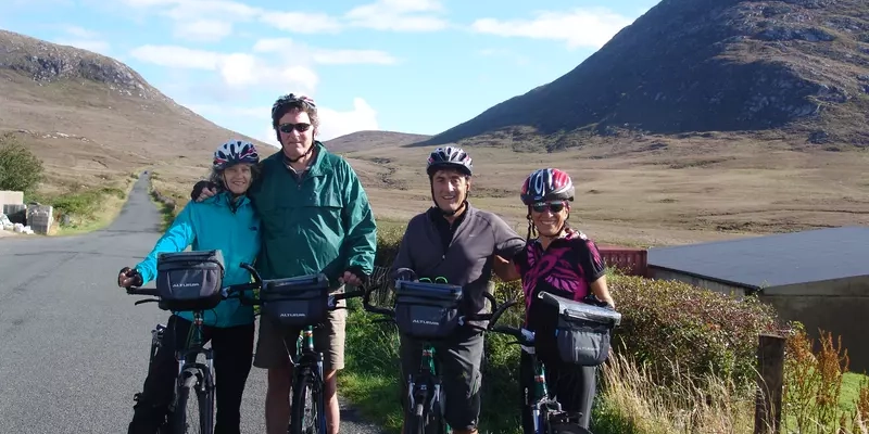 4 cyclists on a rural road with mountains on each side.
