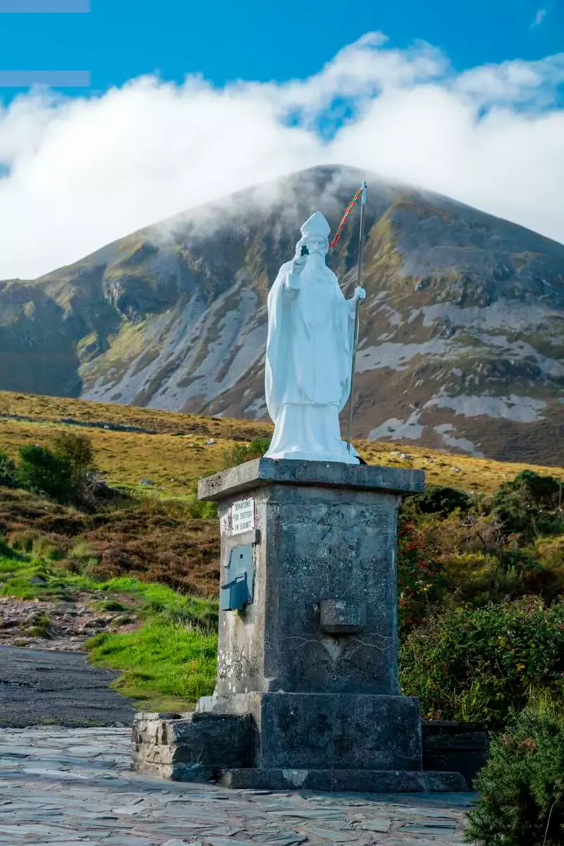 White Statue on pedestal with mountain in the background.
