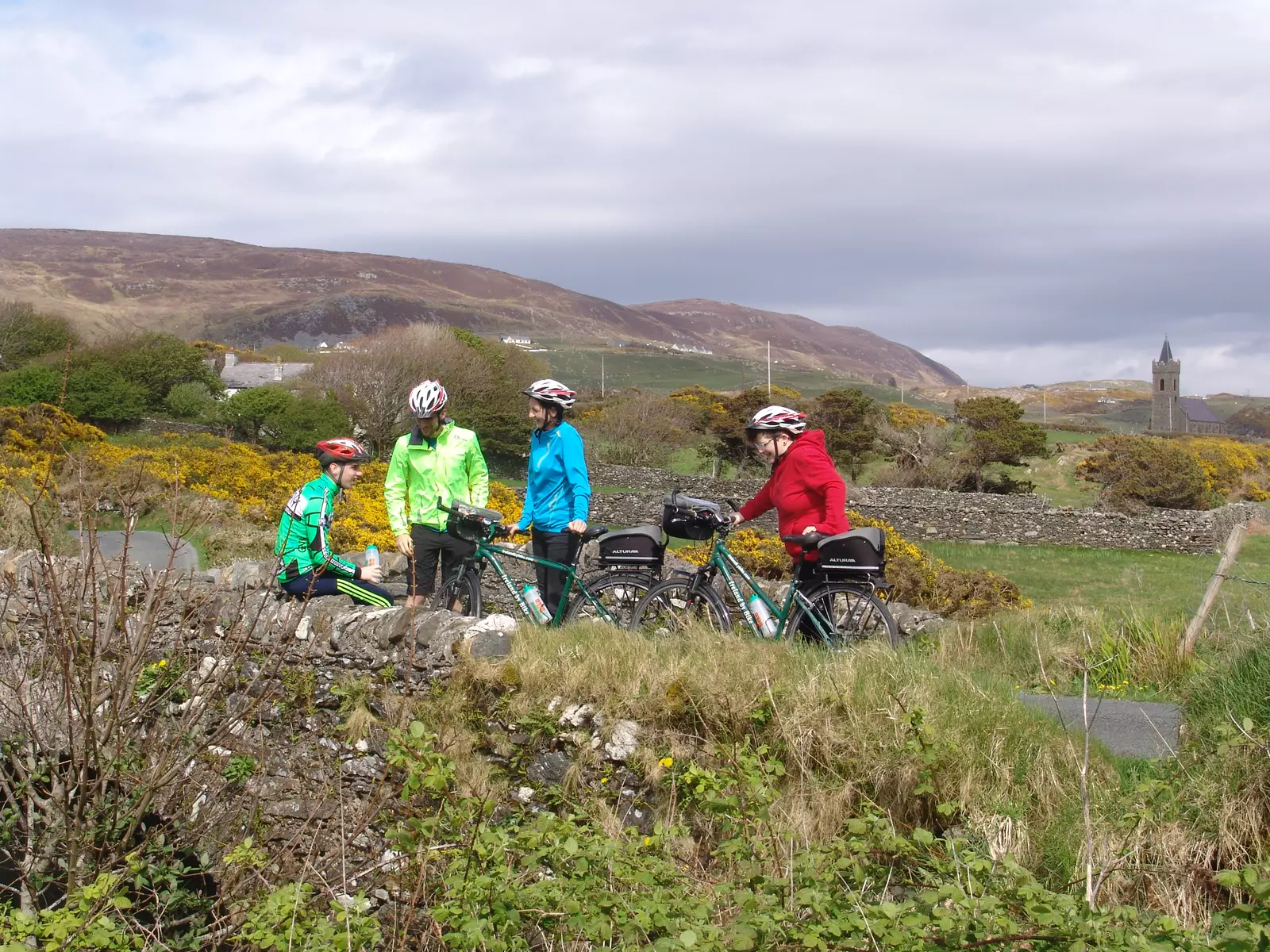 4 cyclists wearing bright colours sitting or standing on a stone bridge