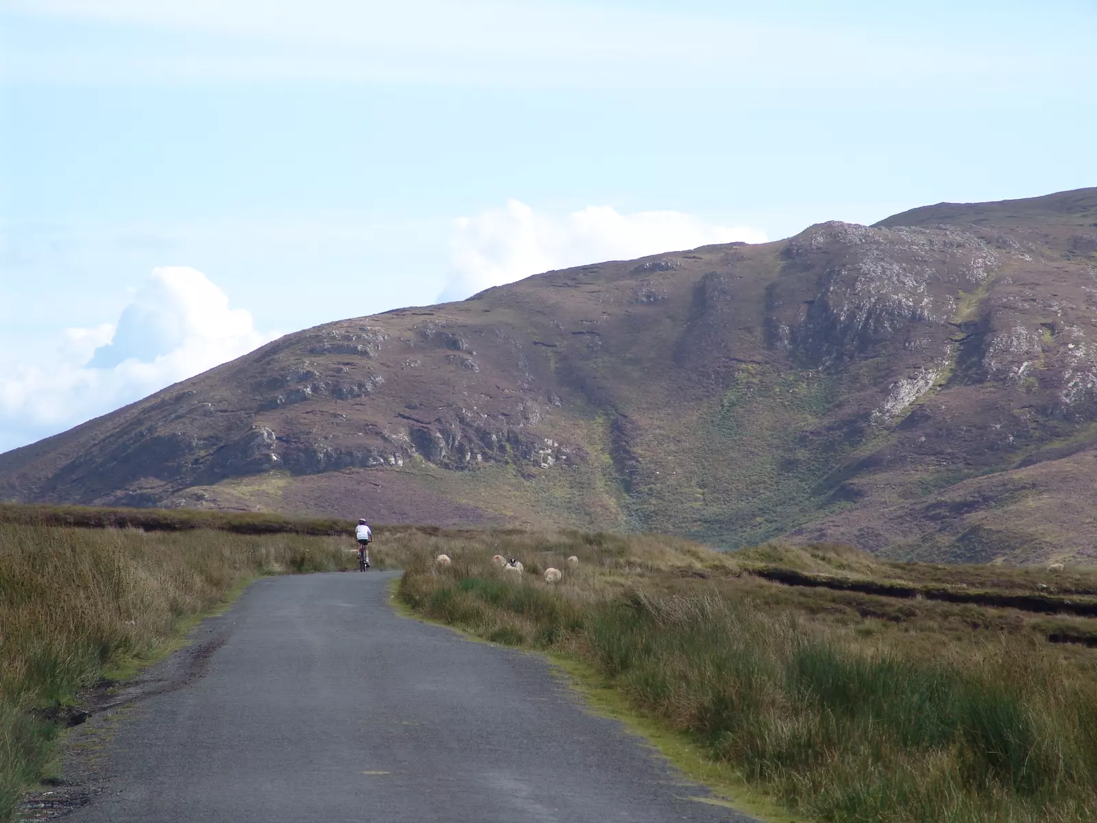 Cyclist on country road leading towards a mountain.