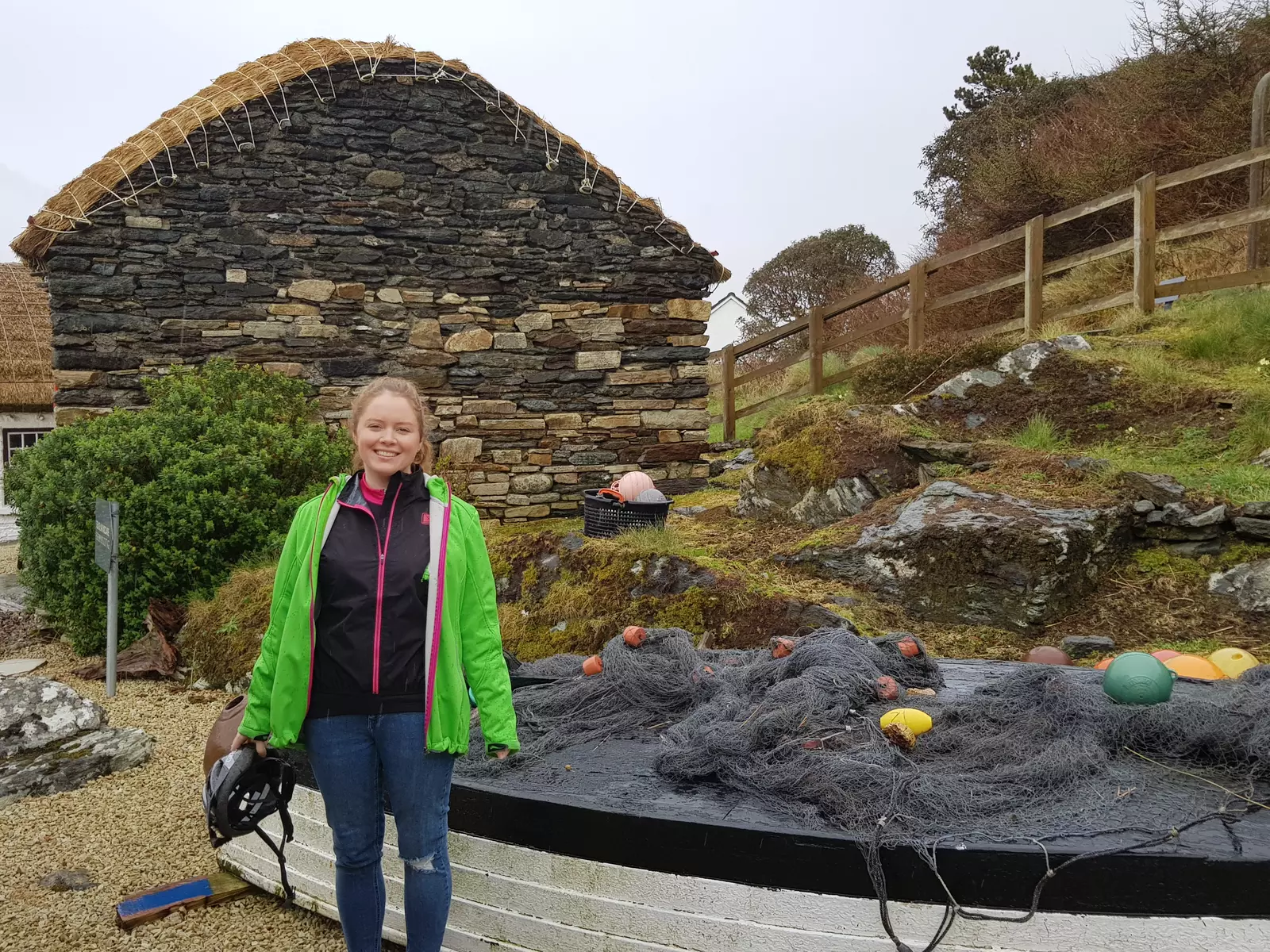 Girl holding cycling helmet beside old stone building with fishing nets on the ground.