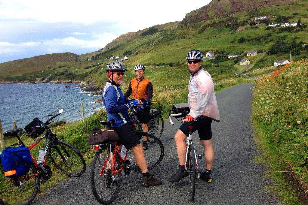 3 cyclists standing with bicycles on narrow road by coast.