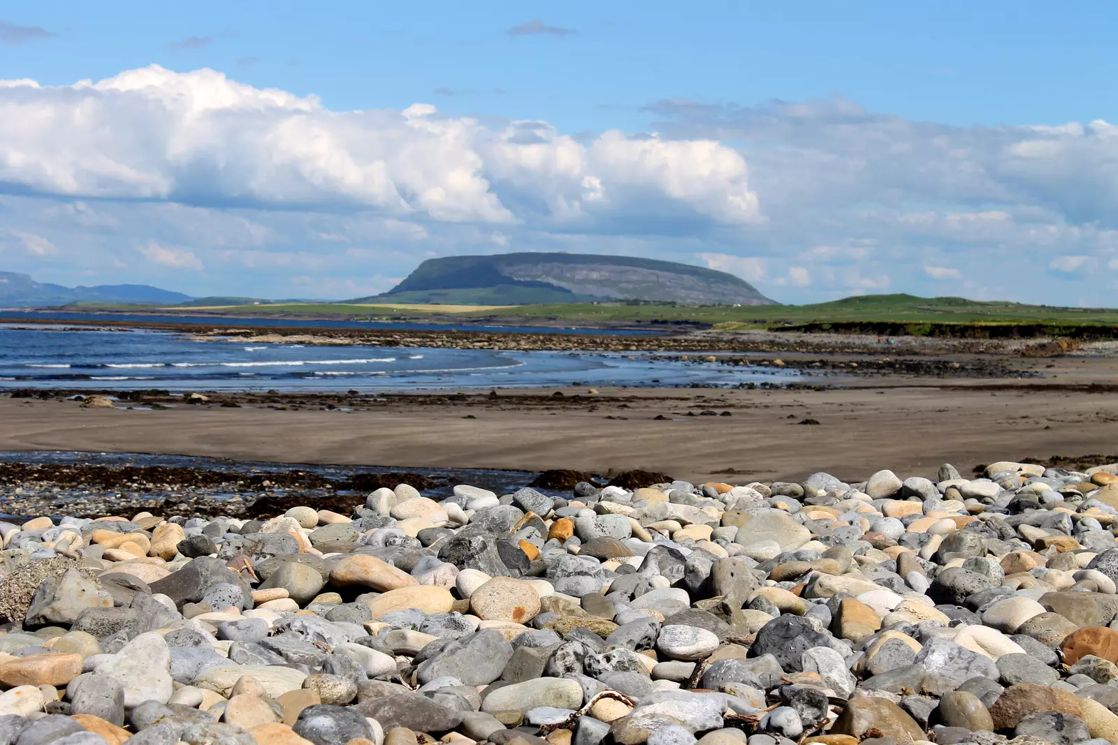 View of hill with bay and sandy beach in front.