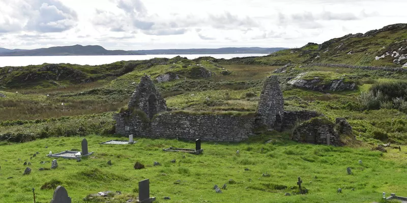 Ruin with gravestones and sea in the distance.
