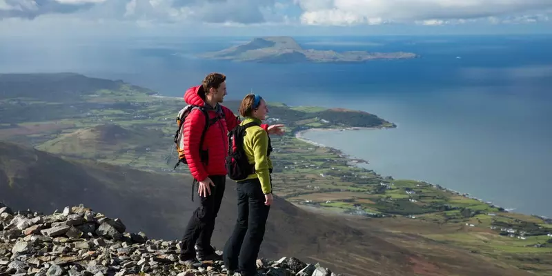 Two hikers on top of a mountain looking out over the sea.