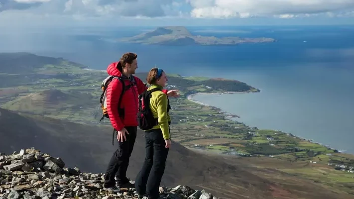 Two hikers wearing rucksacks looking out over coast