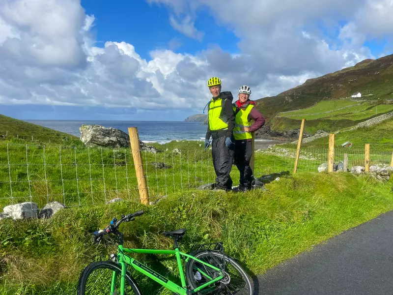 2 cyclists standing by roadside with bike in front