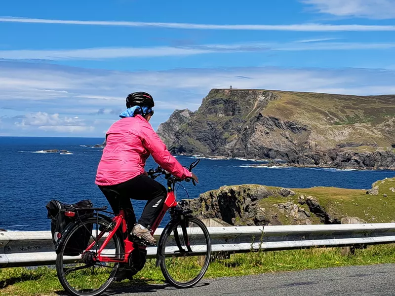 Cyclist wearing pink cycling past sea cliffs