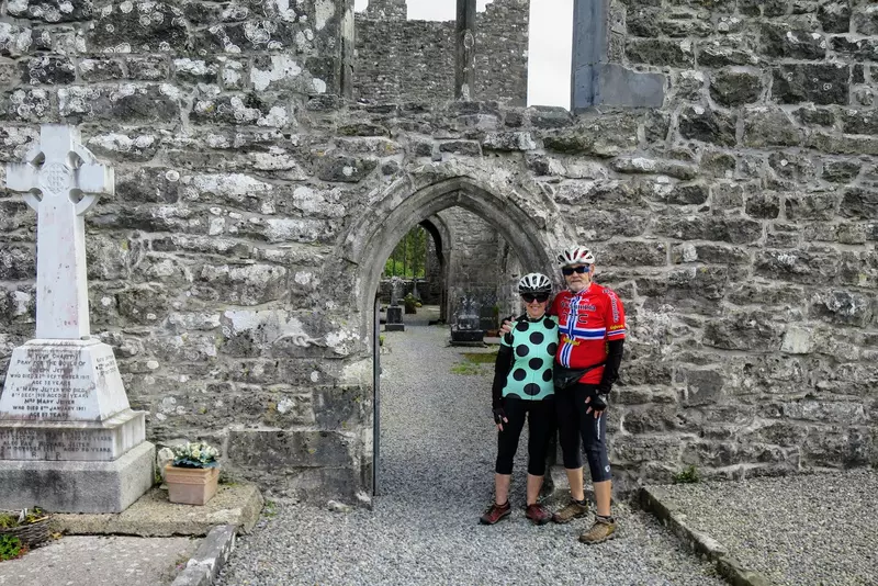 Two people dressed in cycling clothing standing at the entrance to historic building